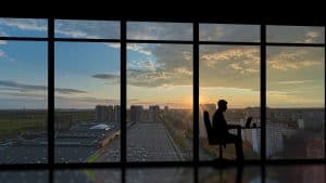 The businessman sitting near the panoramic window with a city sunset