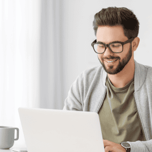 A smiling man using a laptop at home, engaged in online learning classes with a focused and productive mindset.